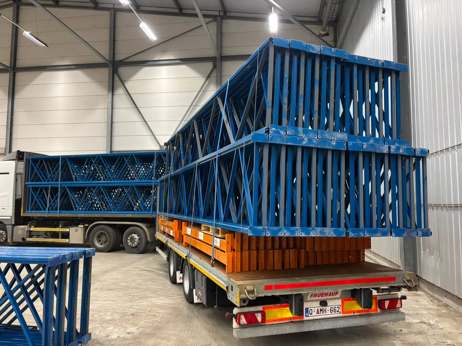 Blauwe staanders van gedemonteerde palletrekken gestapeld op een oplegger in een lege hal