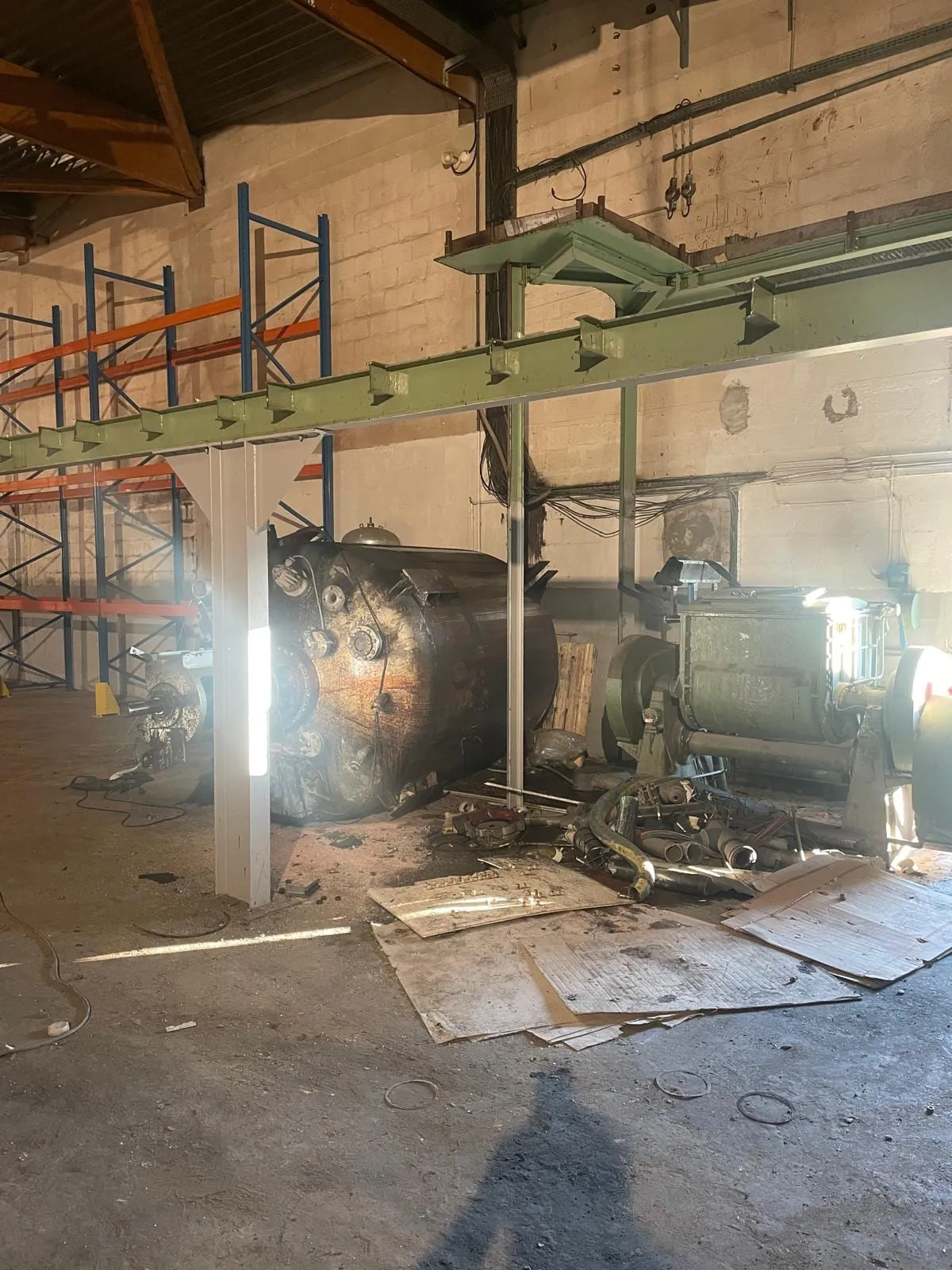 Fabriekshal tijdens de afbraakfase: een oude drukketel en een industriële menger onder een kraanbaan, met palletstellingen in ontmanteling op de achtergrond