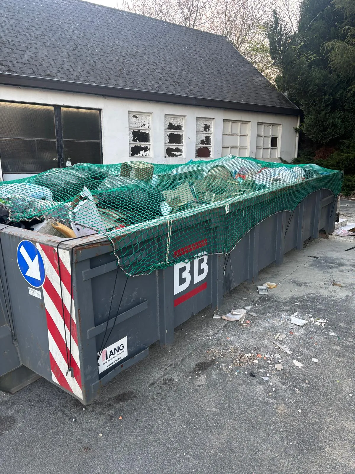 Volle afvalcontainer van BB Racks onder een net bij een ontruiming