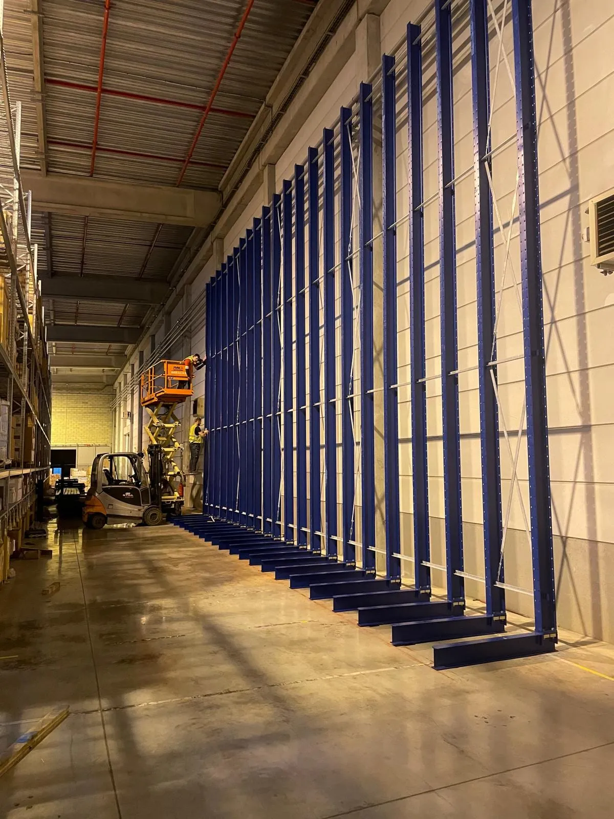 Blauwe draagarmstelling tegen de magazijnwand, met schoren en verstelbare armen