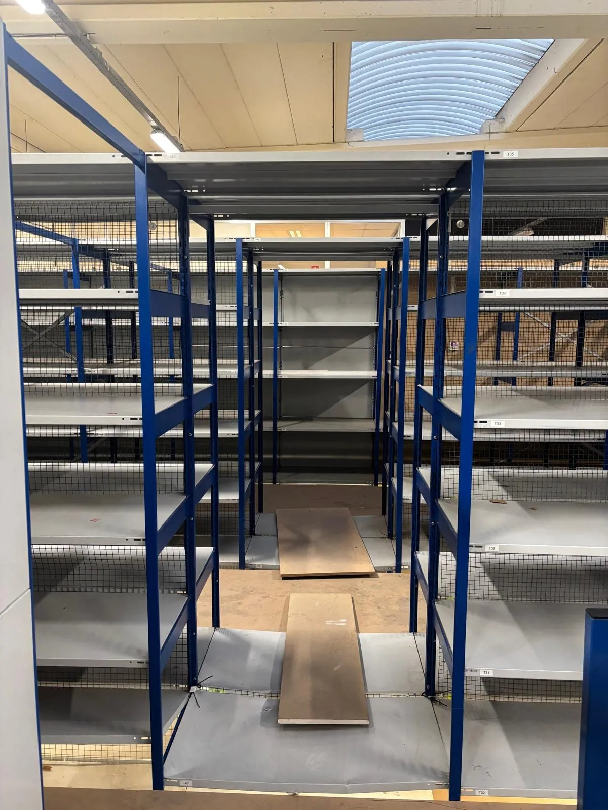 Gang tussen blauwe legbordstellingen in de berging, rekken grotendeels leeggehaald
